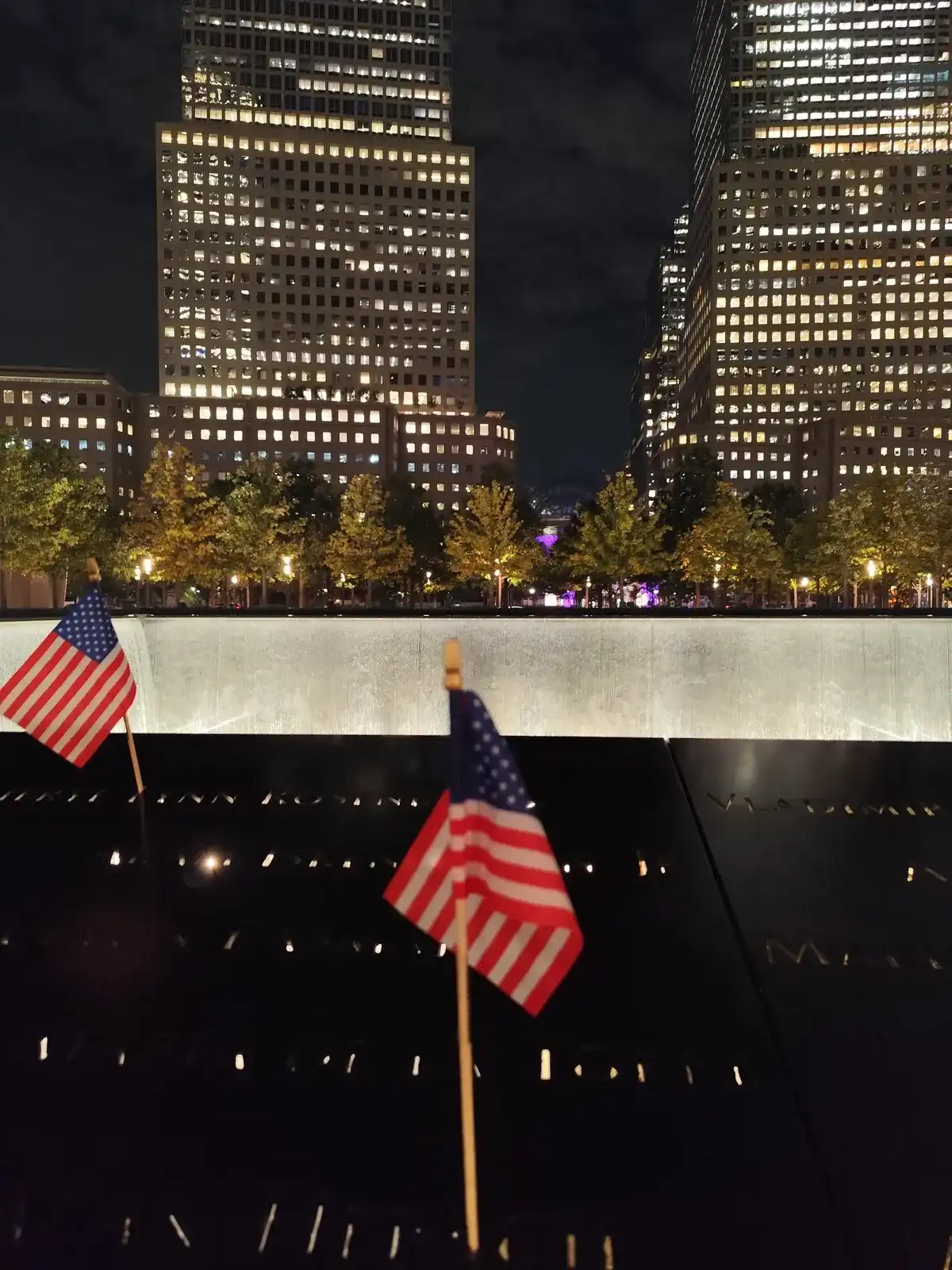 Bassin van het 9/11 Memorial bij nacht met Amerikaanse vlaggetjes in de namen van de slachtoffers