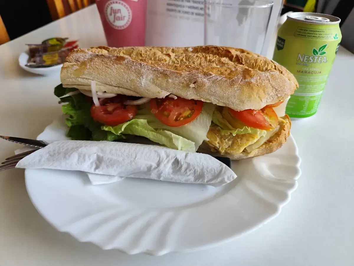 Bocadillo de pan con lechuga, tomate y queso en un plato blanco, con una lata de Nestea