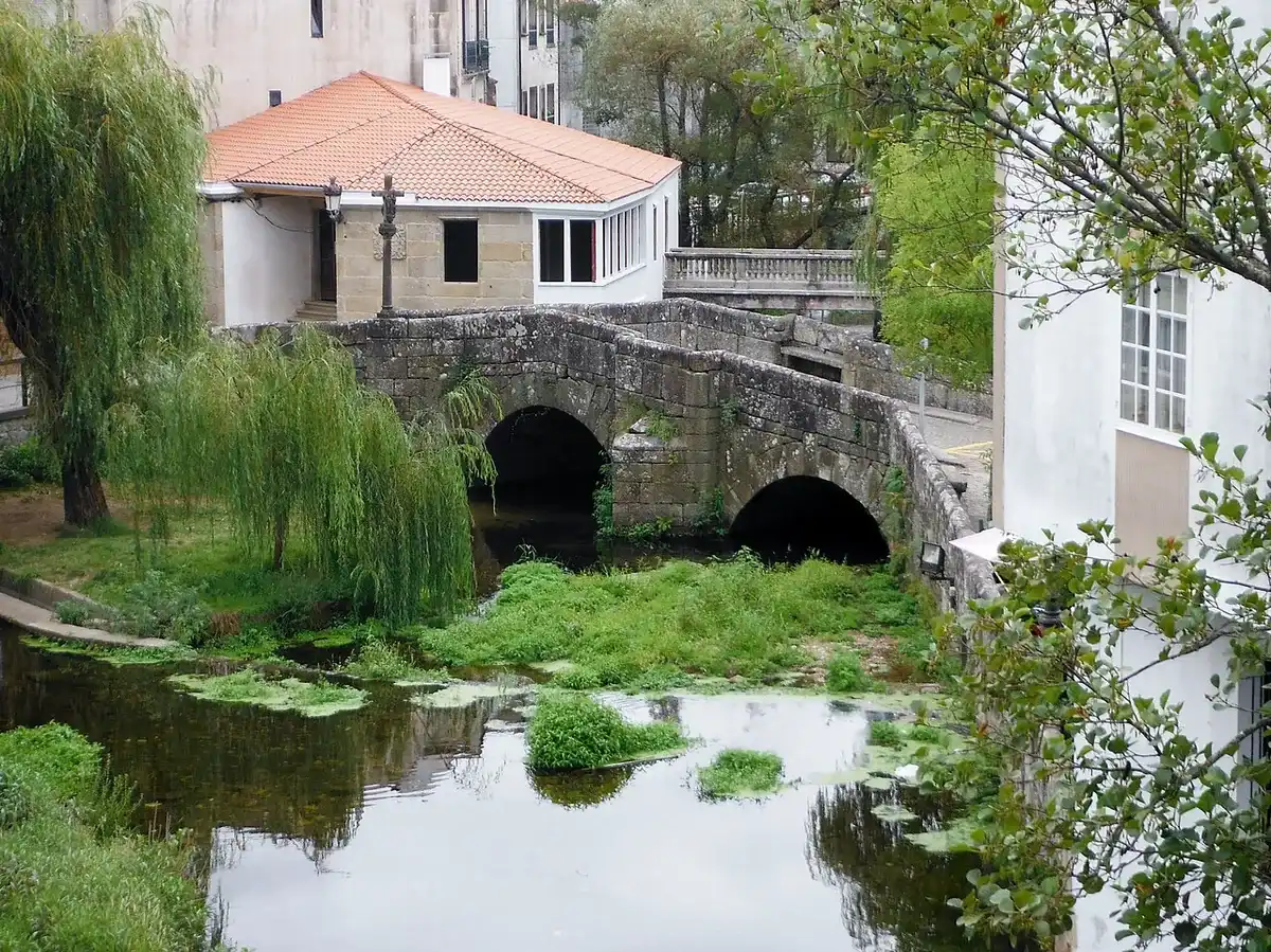 El puente de piedra de dos arcos con su cruceiro sobre el río Bermaña, en Caldas de Reis