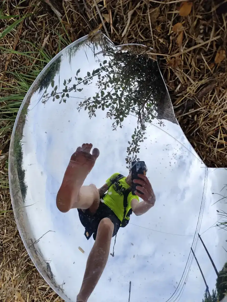 Michiel Das con mochila caminando descalzo, reflejado en un espejo de carretera junto al Camino