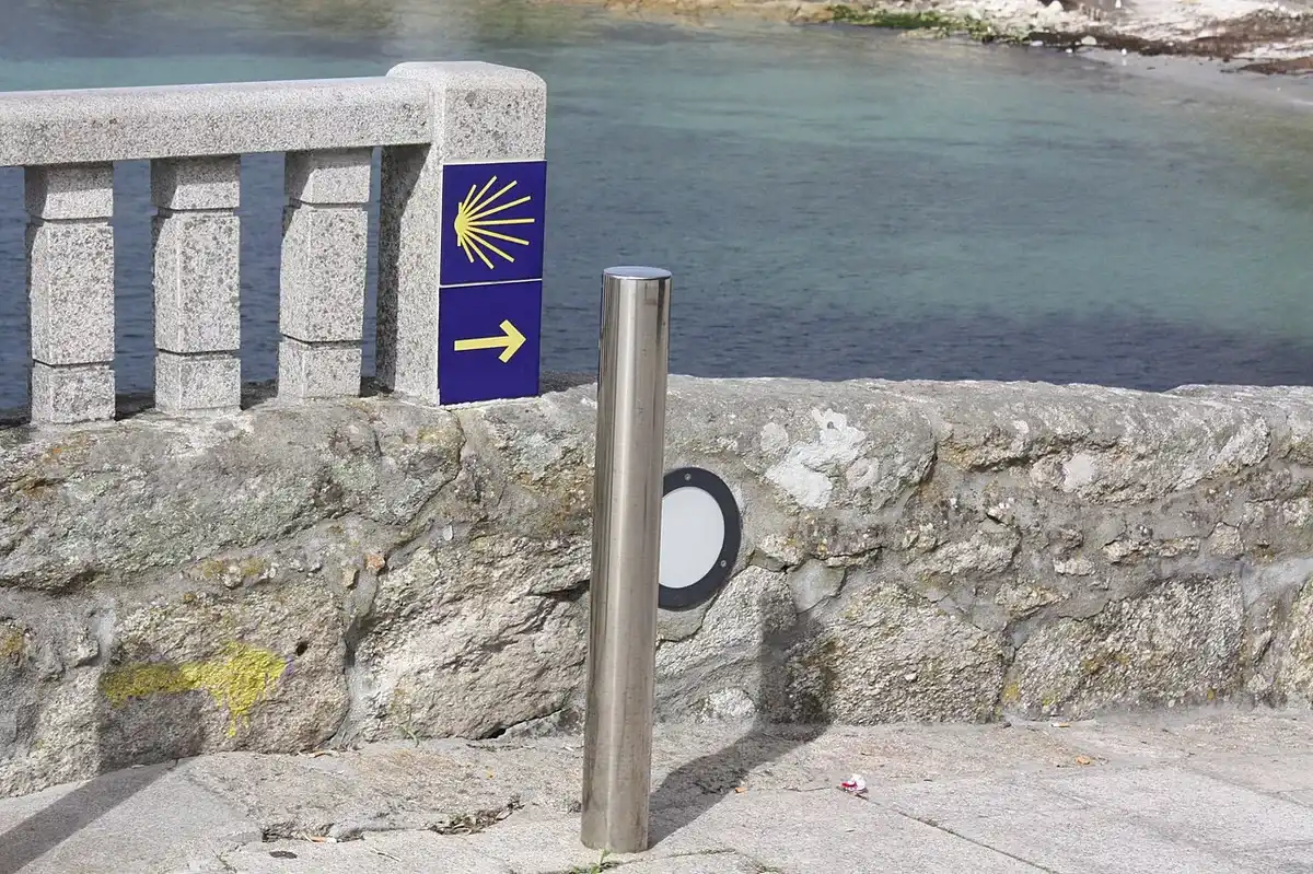 Señal azul del Camino Portugués de la Costa con la concha y la flecha amarillas, sobre un muro junto al mar en Oia