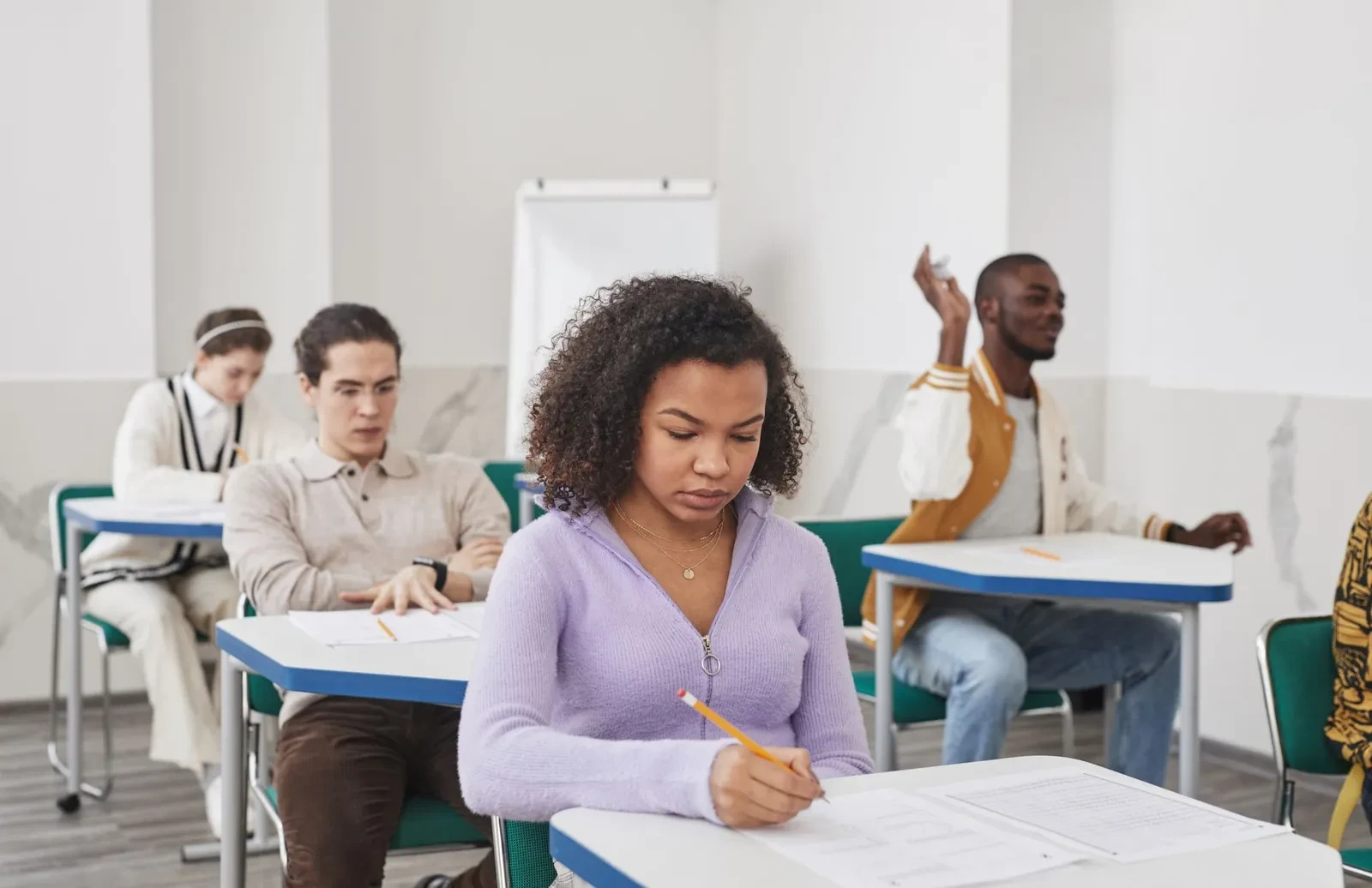 Mensen die aan tafeltjes een schriftelijk examen afleggen in een examenzaal
