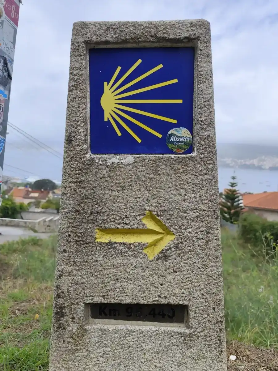 Mojón de piedra del Camino con la concha y una flecha amarilla