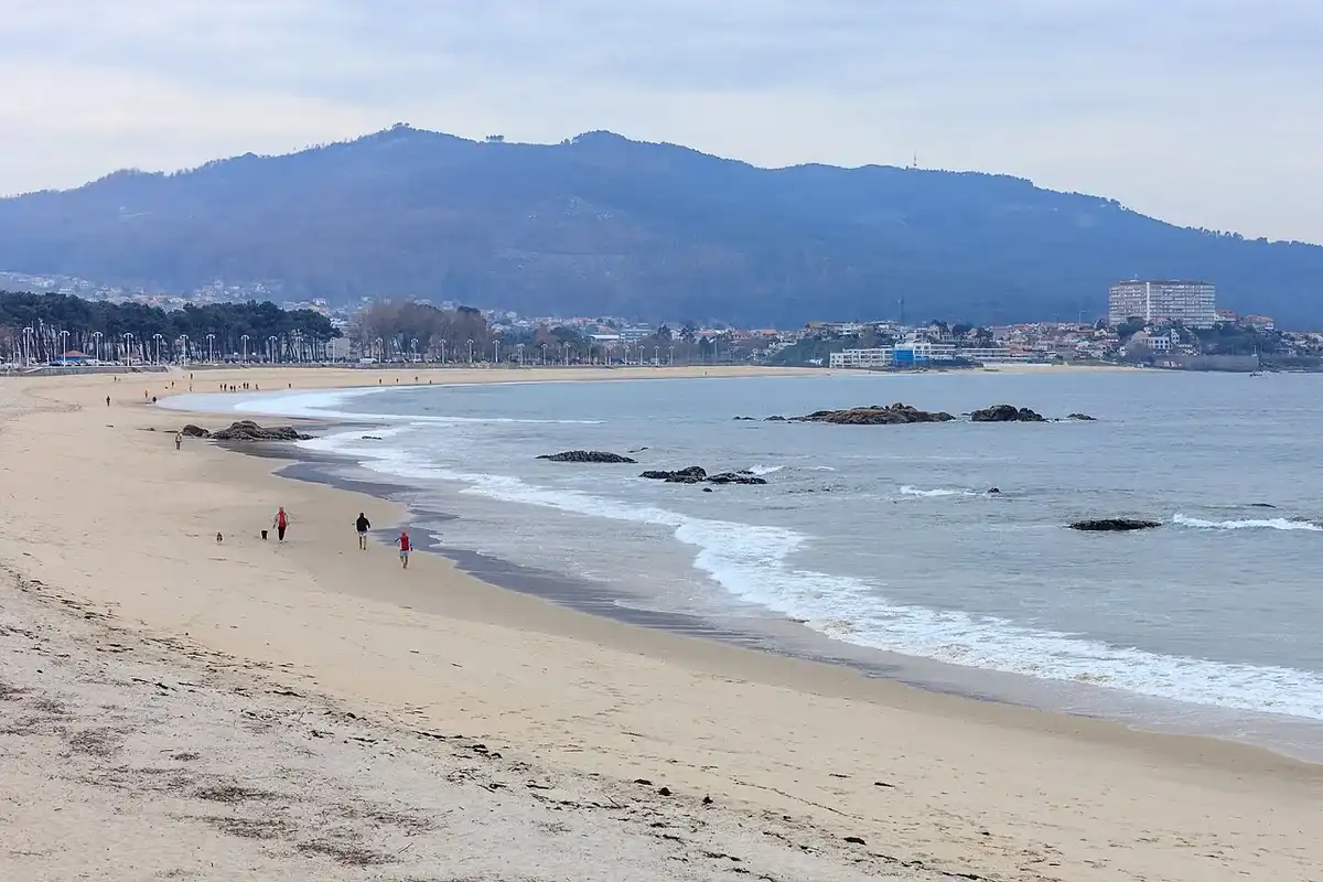 La playa de Samil, en Vigo, con rocas en el agua y la ciudad al fondo