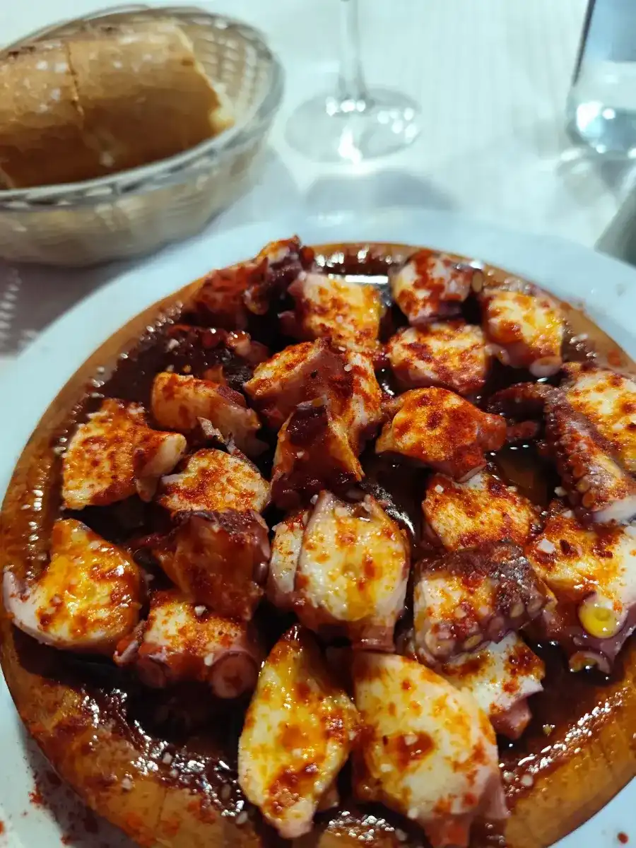 Pulpo a feira con pimentón y aceite en un plato de madera