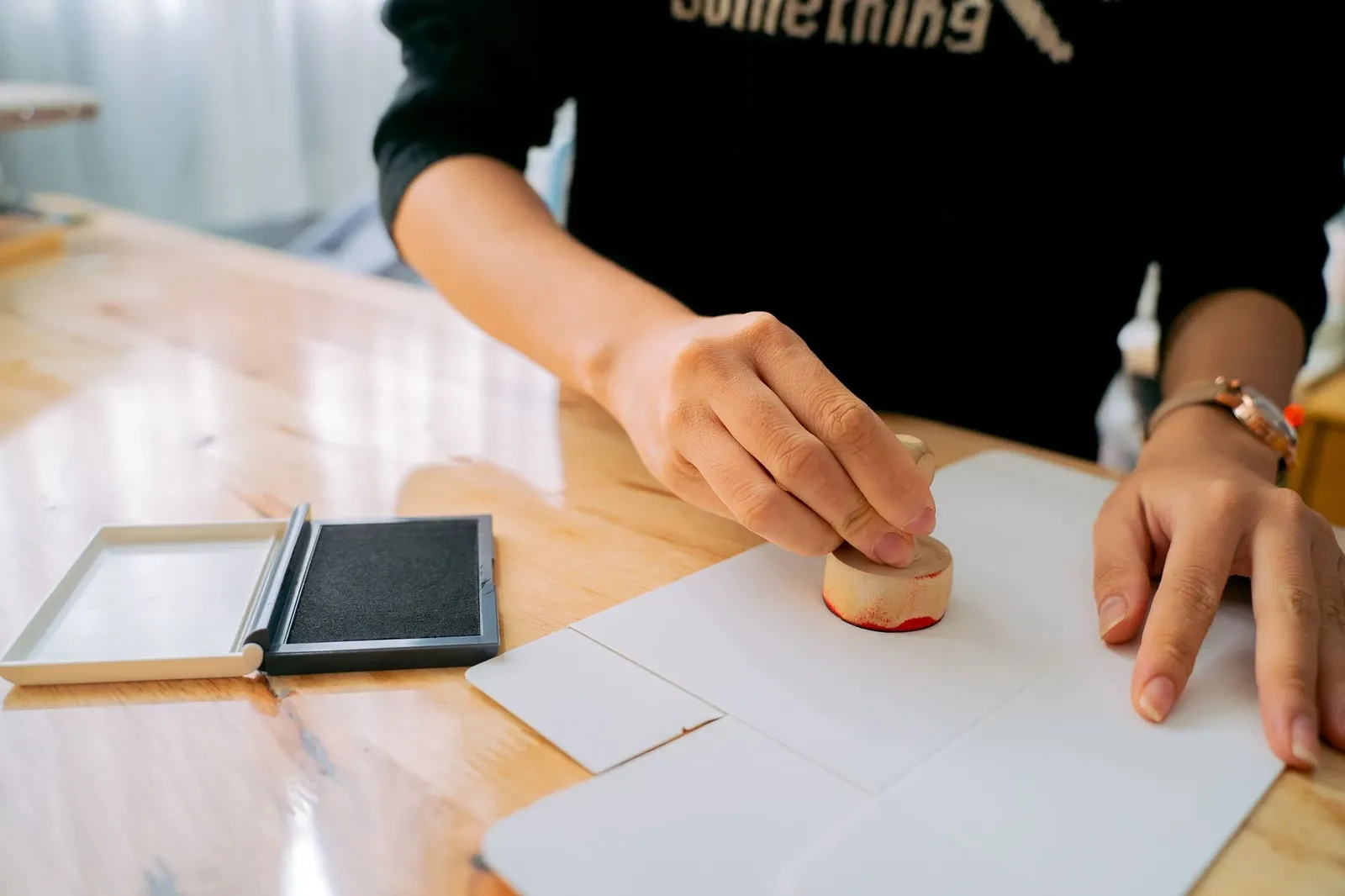 Een hand die een stempel op een document zet aan een bureau